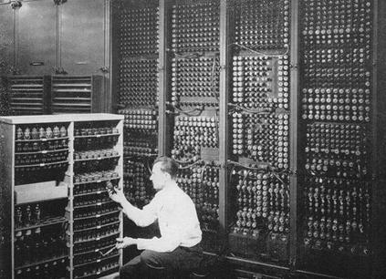 A technician kneeling to replace a vacuum tube inside ENIAC, an early binary computer